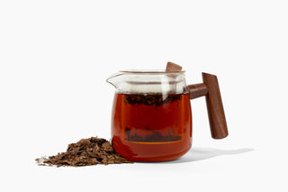 Tea pot with wooden handle filled with tea leaves and brewed tea on a white background
